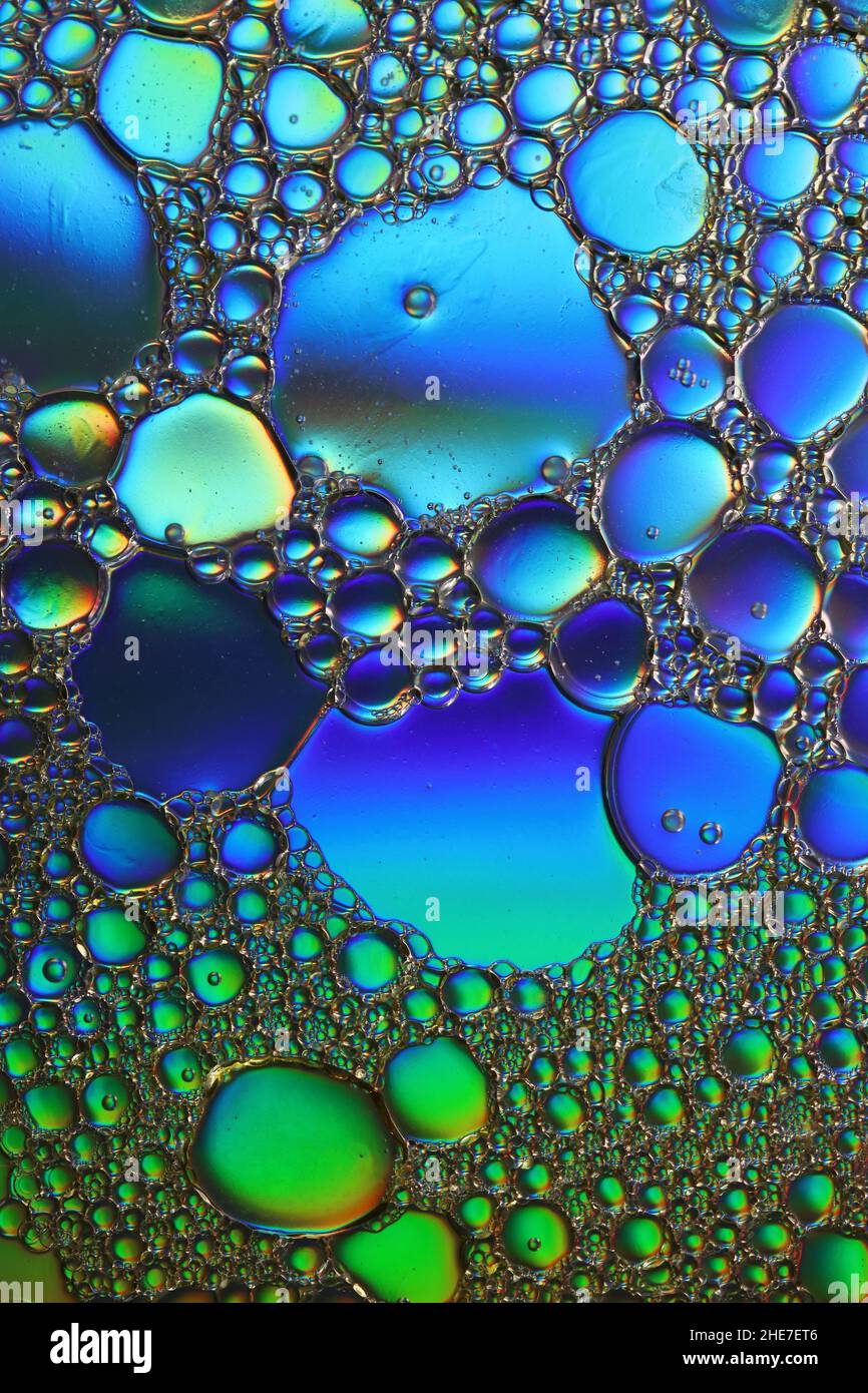 Grün und blau beleuchtete Öltröpfchen schweben auf einer Wasseroberfläche, Makrofotografie Stockfoto