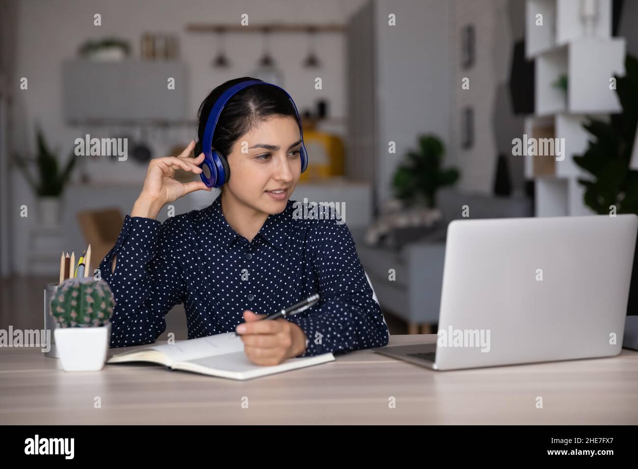 Fokussiertes lächelndes indisches Studentenmädchen in Kopfhörern, das von zu Hause aus studiert Stockfoto