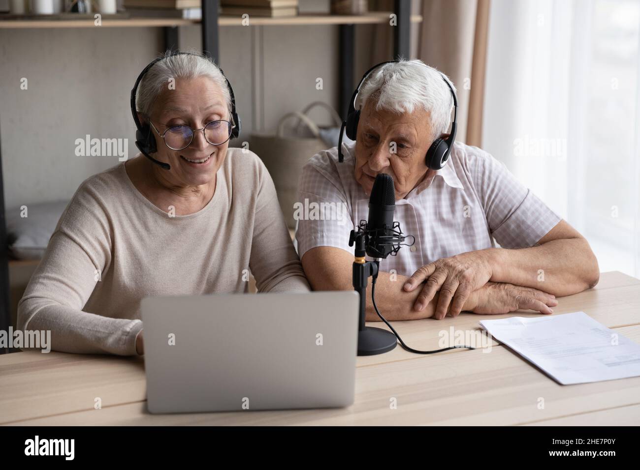 Freudig fokussiertes altes Paar, das zu Hause eine Stimme aufzeichnete. Stockfoto