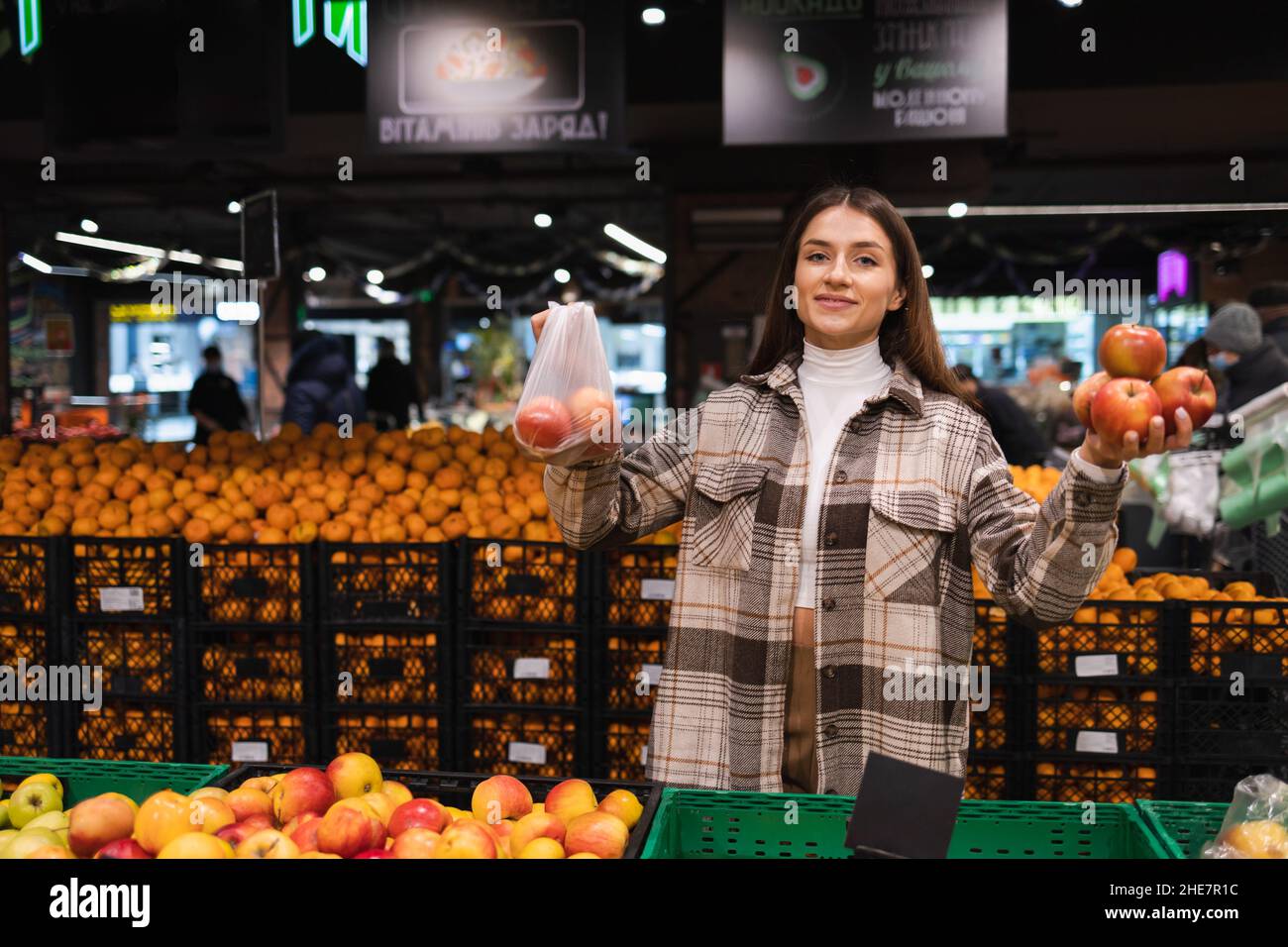 Die Frau denkt darüber nach, ob sie Äpfel in einer Plastiktüte nehmen oder nicht. Mädchen kauft Obst in einem Supermarkt. Konzept einer Welt ohne Plastik Stockfoto