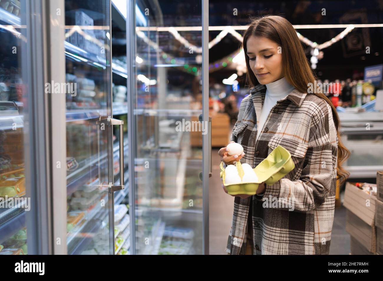 Die junge Frau kauft Hühnereier in einem Supermarkt. Mädchen im Lebensmittelgeschäft Stockfoto