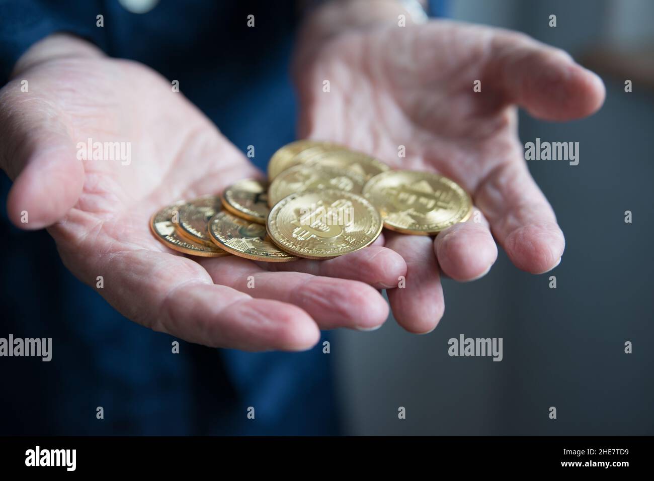 Hände eines gealterten Mannes, der viele goldene Münzen hält und zeigt, die Bitcoins darstellen. Konzeptinvestition in Kryptowährungen. Spanien Stockfoto