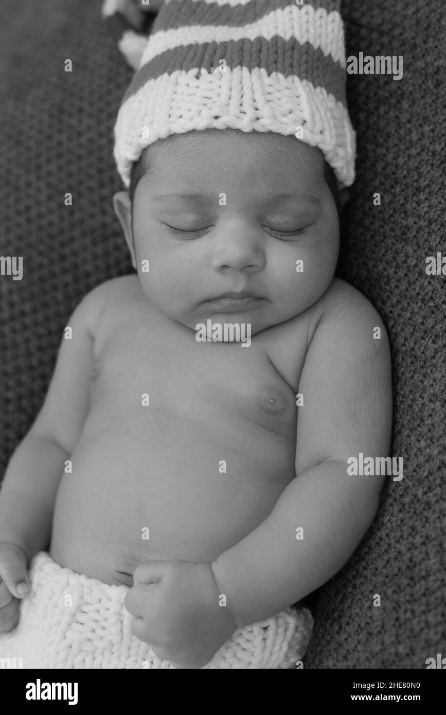 Nahaufnahme des liegenden Neugeborenen in einem gestreiften Hut schläft mit zusammengeklemmten Händen Stockfoto