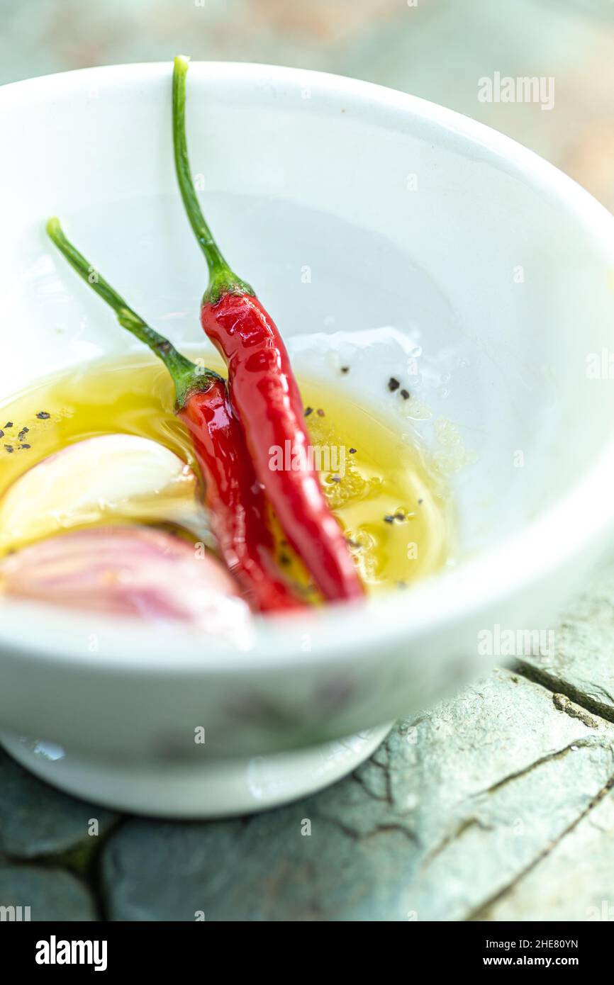 Aromatisches Kräuteröl mit frischen roten Chilis, Knoblauch und Pfeffer Stockfoto