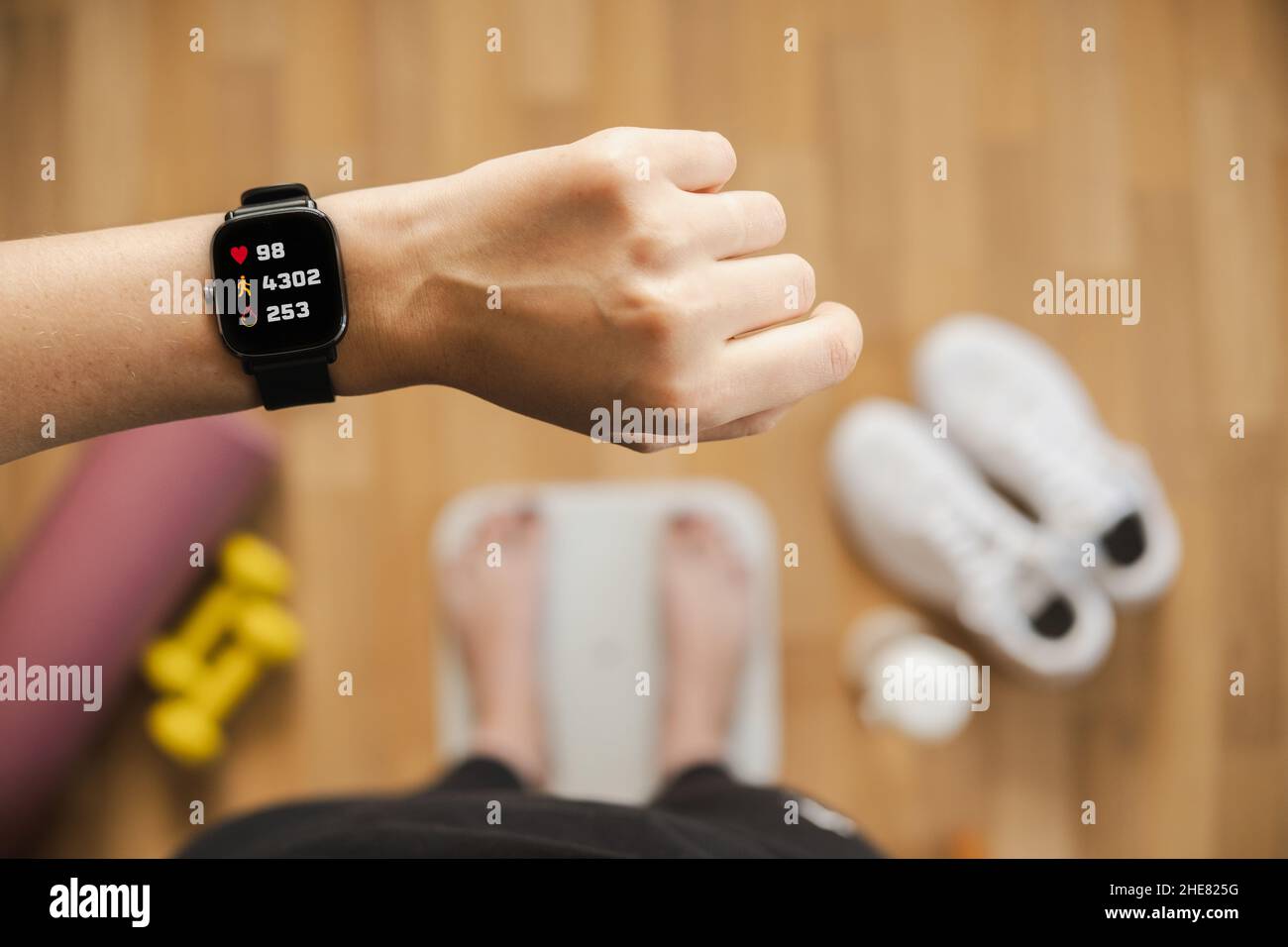 Betrachten Sie den Fitness-Tracker, der die Herzfrequenz, die Schrittzählung und die verbrannten Kalorien anzeigt, während Sie auf der Waage stehen, aus der Sicht der ersten Person. Intelligente Uhr auf weiblichen ha Stockfoto