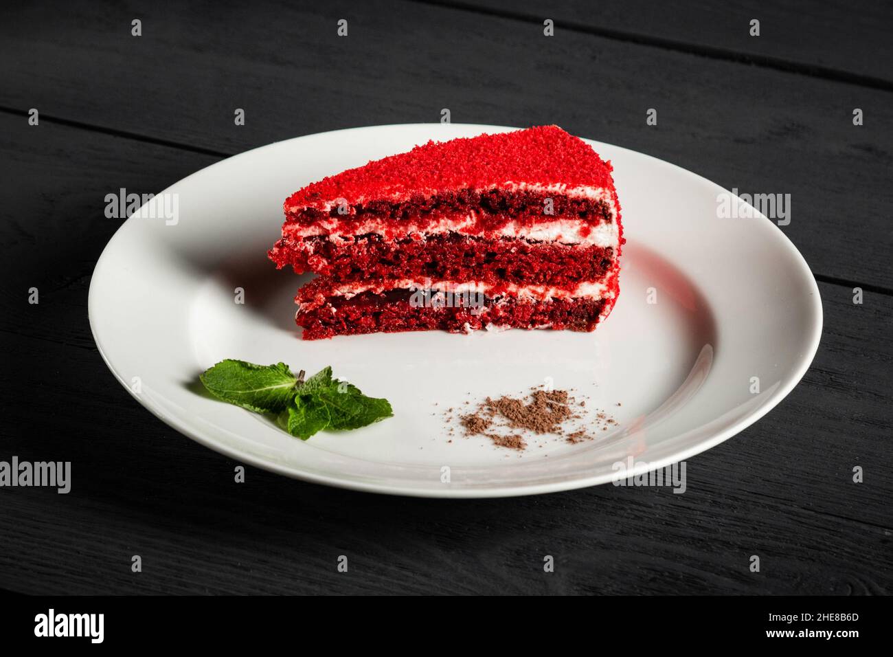 Ein Stück roter Kuchen auf einem weißen Teller. Schwarzer Holzhintergrund. Stockfoto