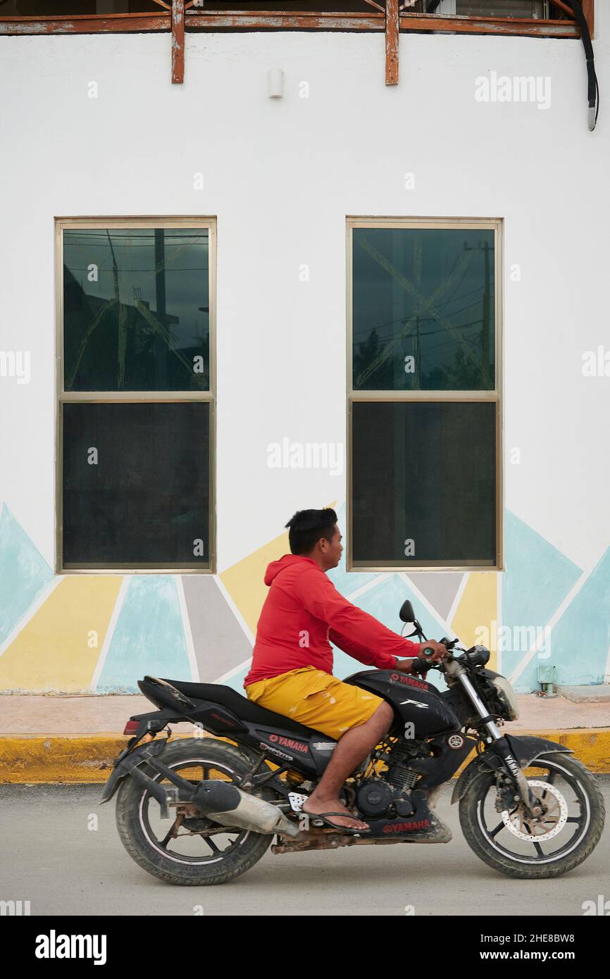 Erwachsener auf einem Motorrad, der vor einem farbenfrohen Gebäude in Chiquila, Mexiko, reist Stockfoto