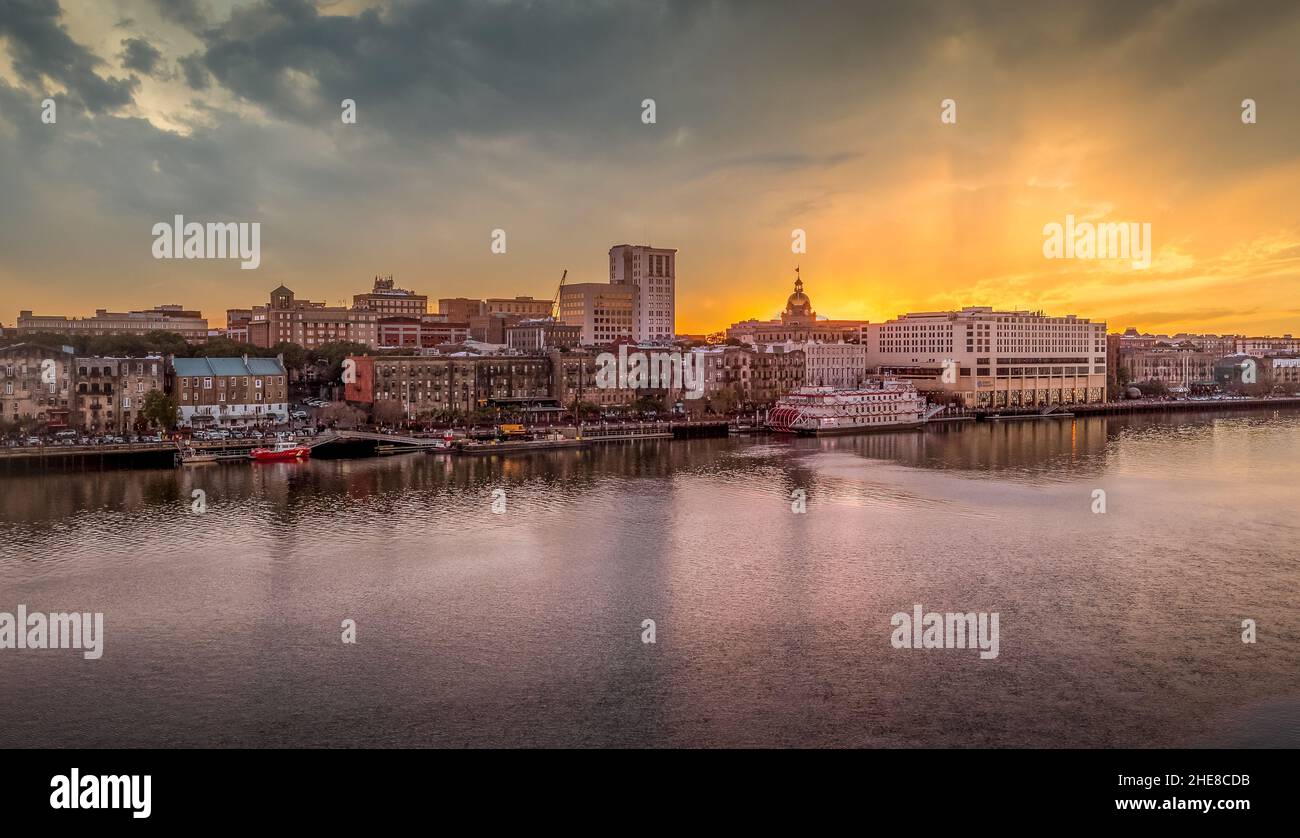 Blick auf den Sonnenuntergang auf Savannah Georgia mit dem Savannah Fluss und den Docks und berühmten Gebäuden am Flussufer, atemberaubendem orangefarbenem Himmel Stockfoto