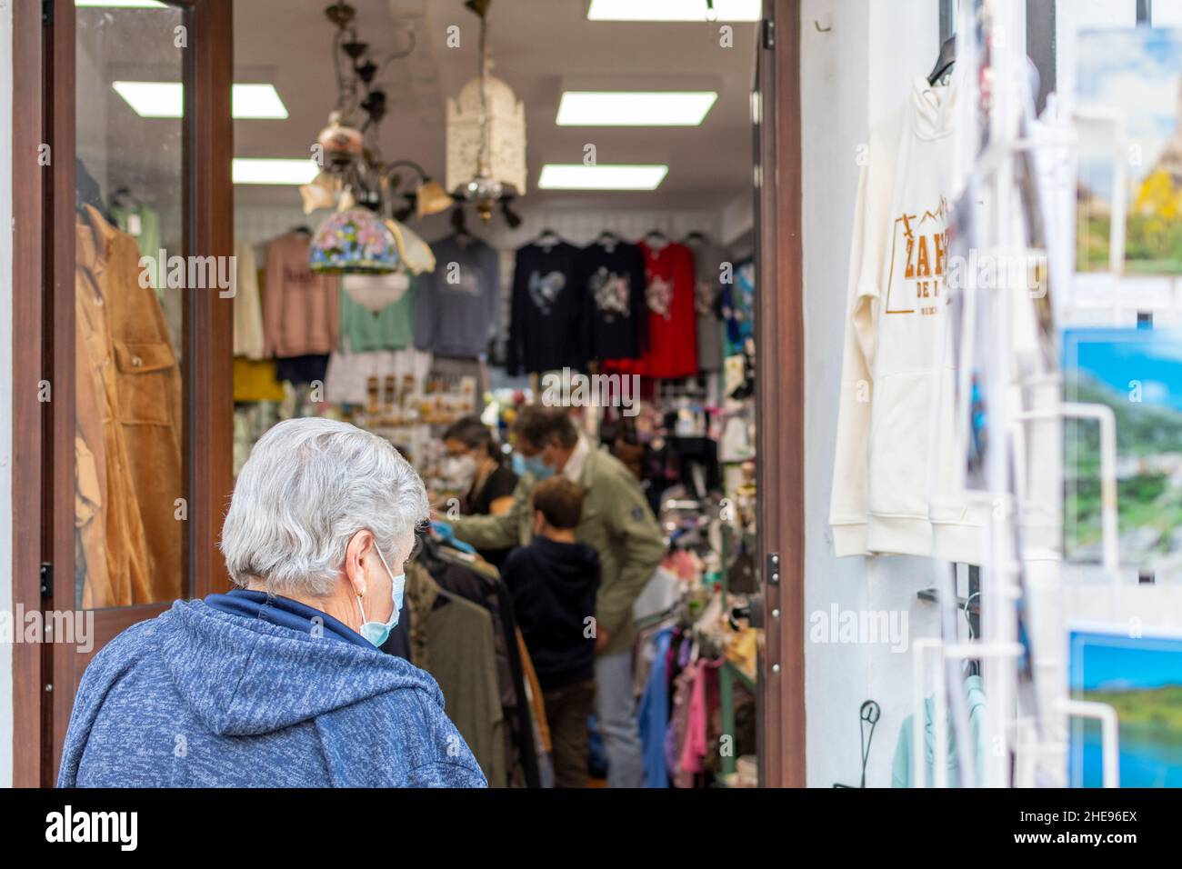 Eine nicht identifizierbare ältere Frau mit einer Maske geht als maskierte Familiengeschäfte in einem Souvenirladen in Zahara de la Sierra, Spanien, ein. Stockfoto