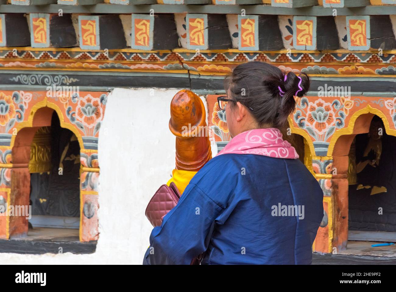 Frau mit einem Holzphallus, die im Chimi Lhakhang (Tempel der Fruchtbarkeit), Punakha, Bhutan betet Stockfoto