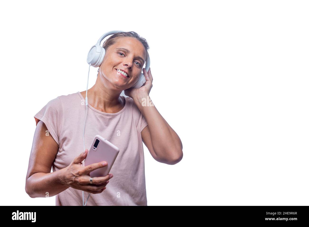 Fröhliche Frau, die Musik hört, mit dem Smartphone, das die Kamera anschaut Stockfoto