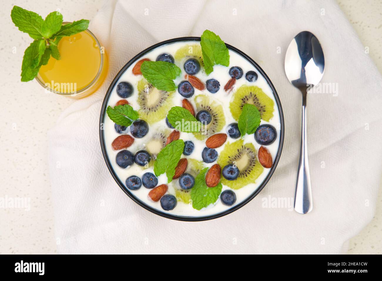 Natürliche und organische Joghurtschale mit Heidelbeeren, Kiwi-Scheiben und Mandeln auf weißem Hintergrund. Draufsicht. Stockfoto