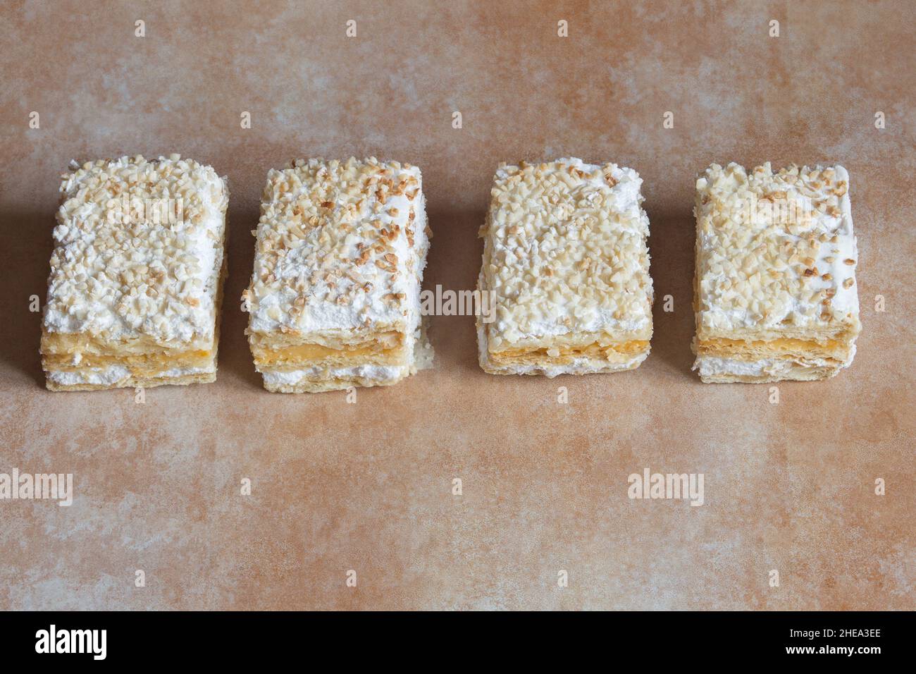 Eine Reihe von einzelnen Portionen Millefeuille aus Blätterteig und gefüllt mit Backcreme und Baiser mit gerösteten gehackten Mandeln und Zucker. Stockfoto