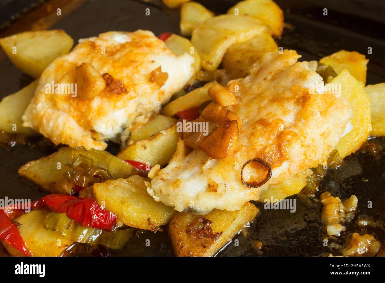 Nahaufnahme von Kabeljau auf einem Backblech, das mit roten Paprika, Kartoffeln und Knoblauch gekocht wird. Fisch und gesunde Lebensmittel. Stockfoto