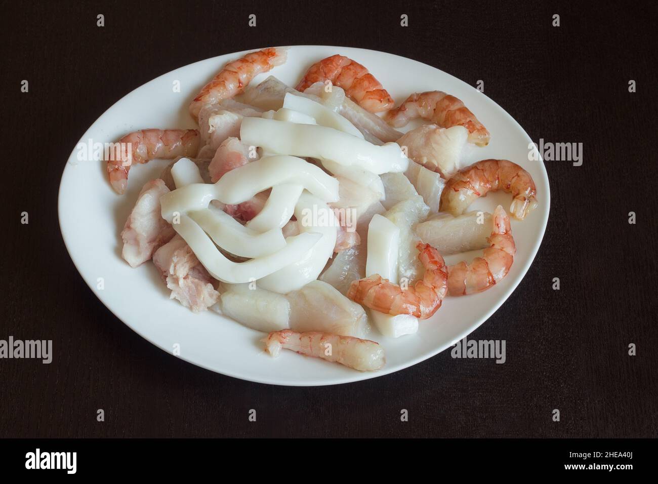 Rohzutaten für die Zubereitung von Meeresfrüchten Auflauf auf einem weißen Teller auf strukturiertem Holz als Hintergrund. Gesunde Ernährung. Stockfoto