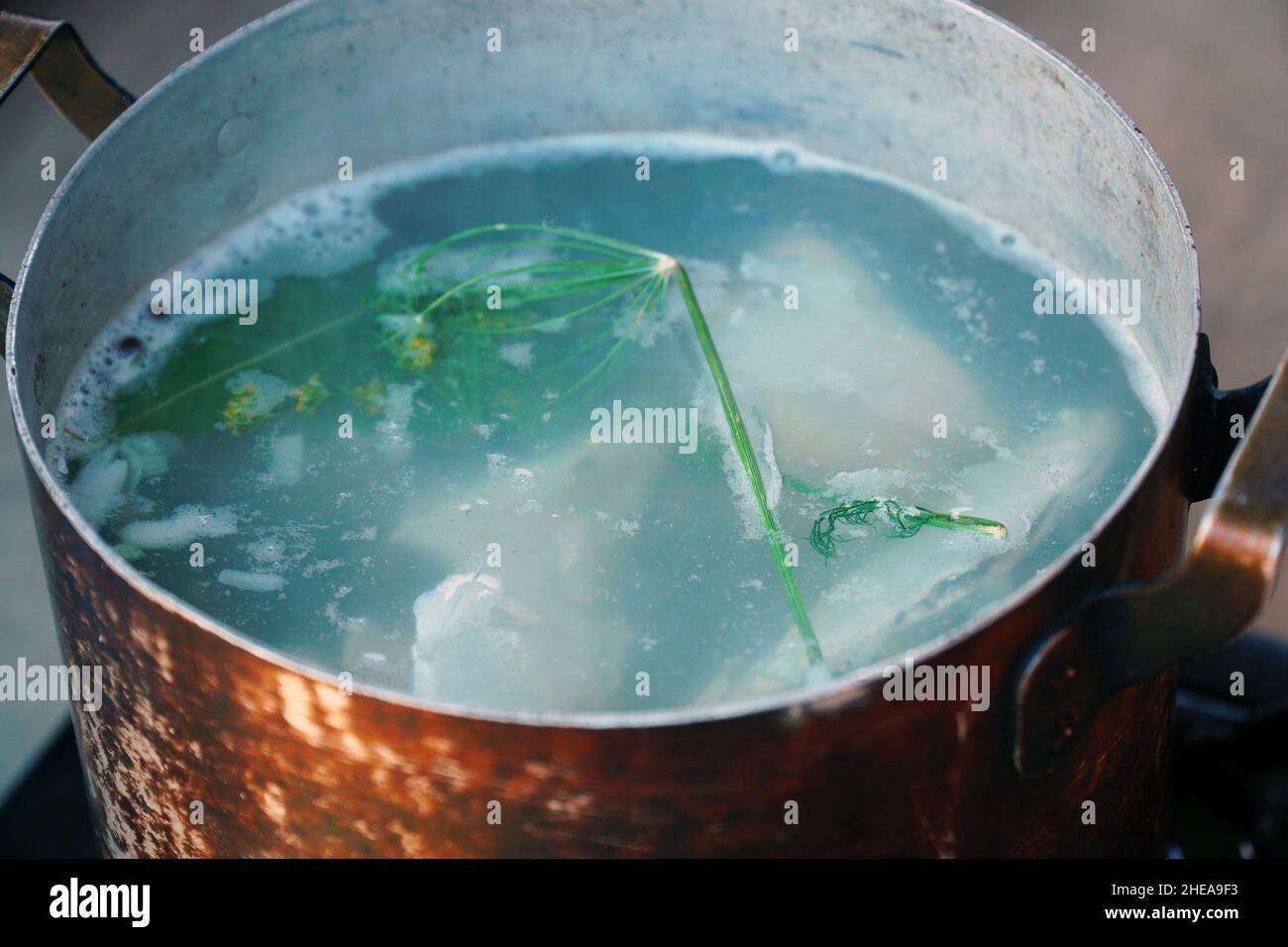 Kochen Fischsuppe in der Natur oder Angeln. Fischsuppenbrühe mit Dill kocht in geräuchertem, geschwärztem Topf Stockfoto