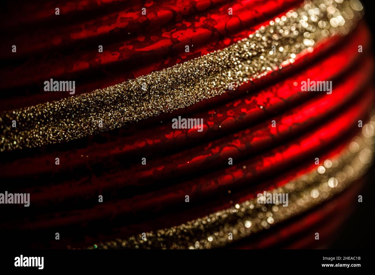 Nahaufnahme einer rot gemusterten Weihnachtskugel mit Glitzerstreifen. Baumschmuck in Rot und Gold. Stockfoto