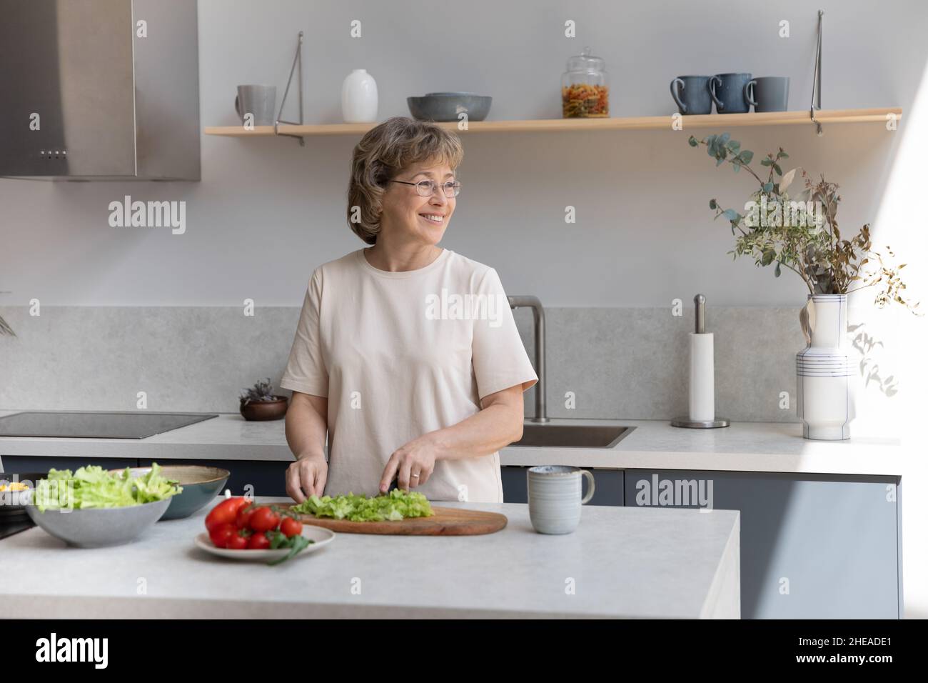 Lächelnde verträumte Frau mittleren Alters, die in der Küche kocht. Stockfoto