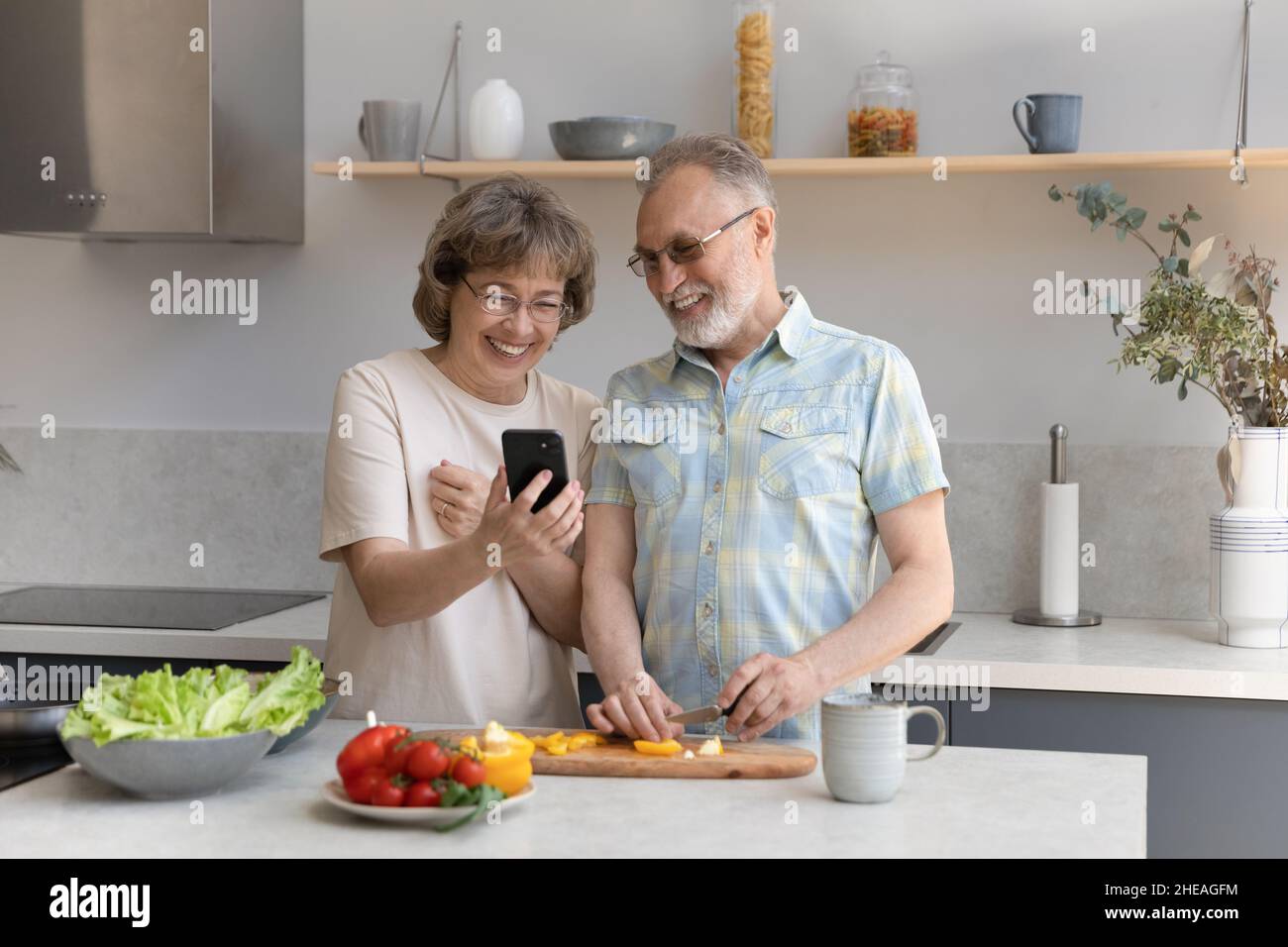 Fröhliches altes Paar, das in der Küche Handy kocht. Stockfoto
