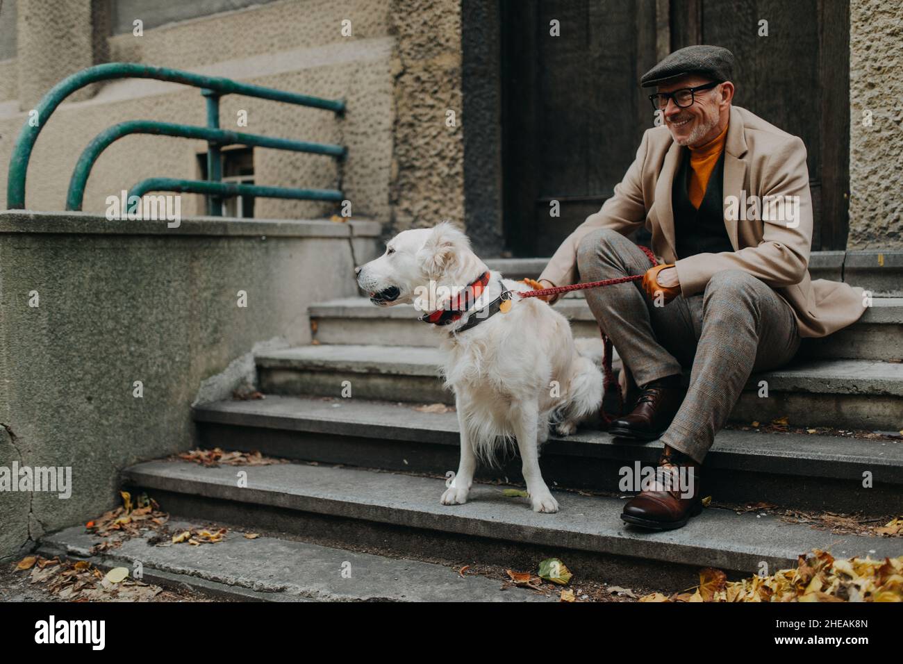 Glücklicher älterer Mann, der auf Treppen sitzt und sich während eines Hundespaziergangs im Freien in der Stadt ausruht. Stockfoto