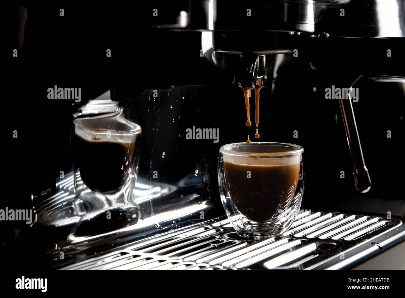 Dunkle Kaffeetropfen tropfen in einer Espressotasse aus transparentem Glas auf einer manuellen Espressomaschine mit Kopierfläche, Nahaufnahme Stockfoto