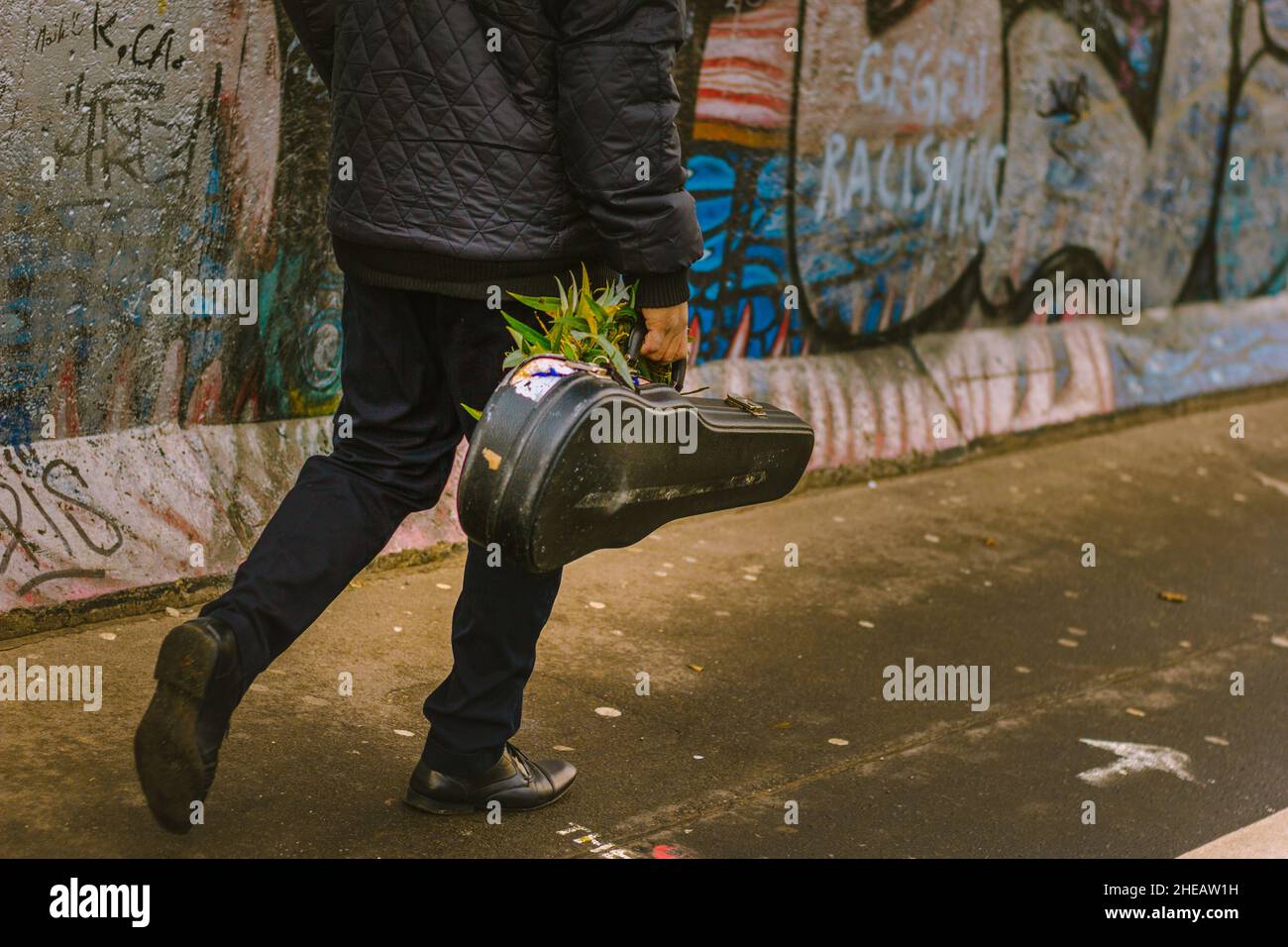 Hombre llevando un violín de la mano delante del muro de Berlín, Alemania Stockfoto