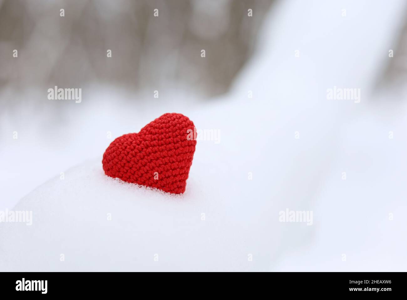Rot gestricktes Herz im Schnee auf Winterwald Hintergrund. Valentinskarte, romantische Liebe Stockfoto