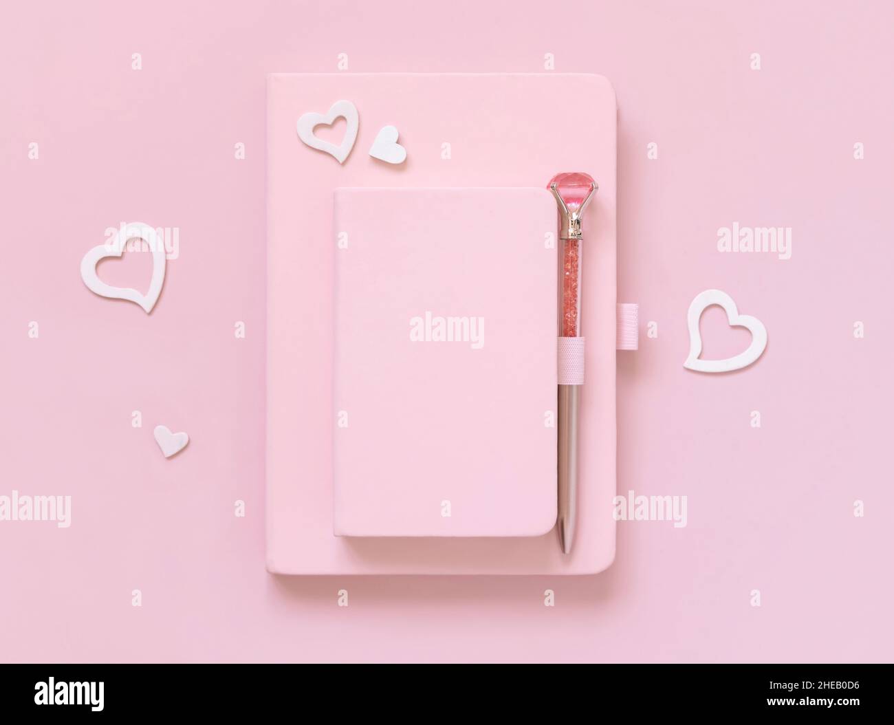 Pinke Hardcover-Notizbücher, dekorativer Edelsteinschreiber und Herzen auf hellrosa Draufsicht. Textbuch-Modell, Planercover mit Platztext. Bildung, Stockfoto