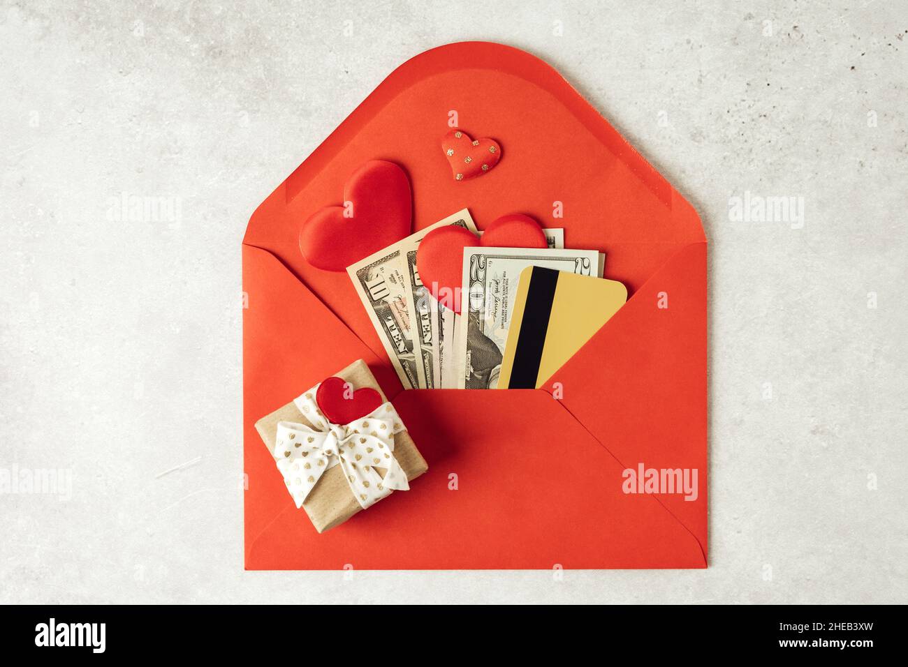 Roter Papierumschlag mit Geldscheinen und Kreditkarte. Flache Lay von grauen Arbeitstisch Hintergrund mit Valentine Geschenk, Brief, Herzform. Oben Stockfoto