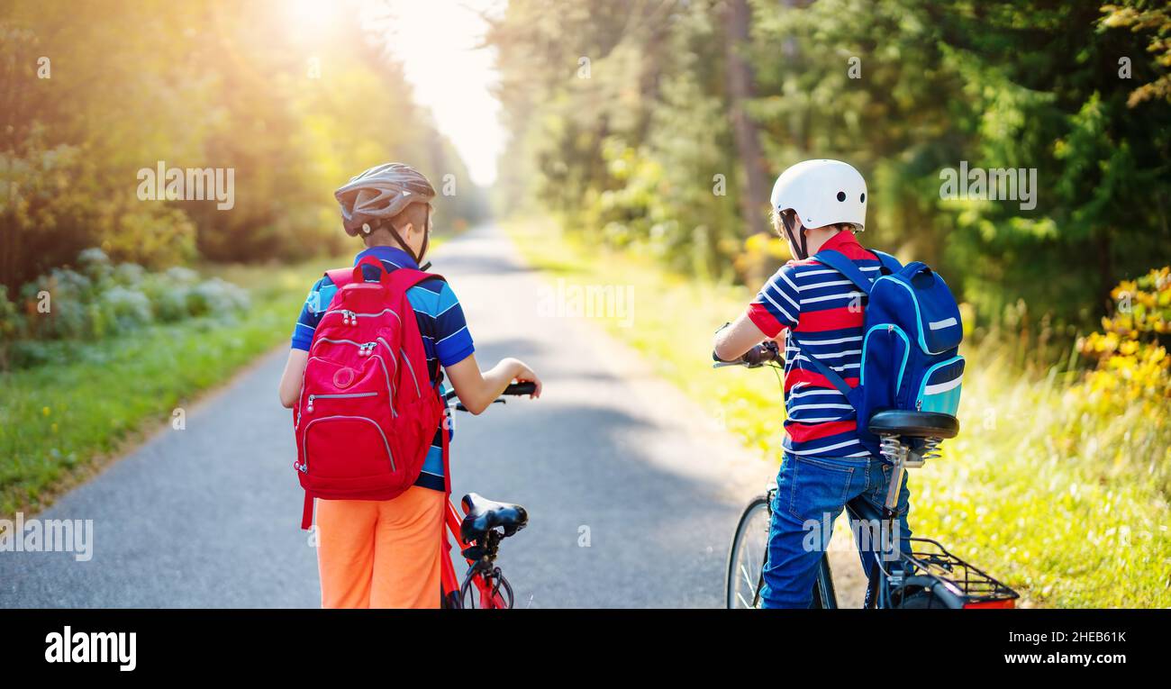 Kinder mit Rucksäcken reiten auf dem Fahrrad im Park in der Nähe der Schule Stockfoto