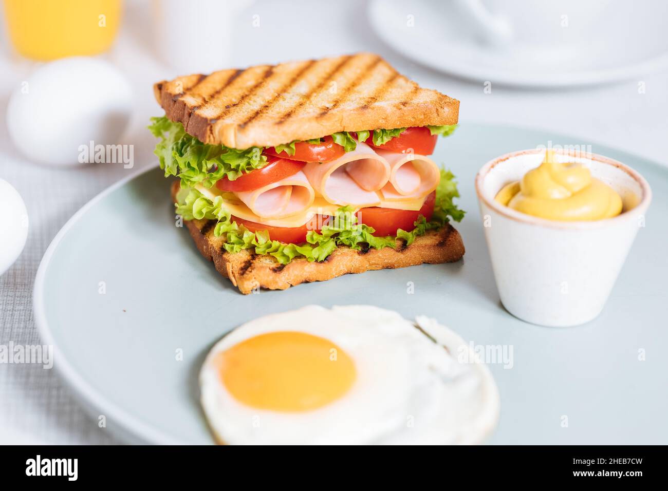 Toast-Sandwich mit gouda-Käse und putenschinken gefüllt mit Tomaten und Salat auf einem hellen Hintergrund mit Zutaten in verschwommenem Hintergrund. Serviert wi Stockfoto