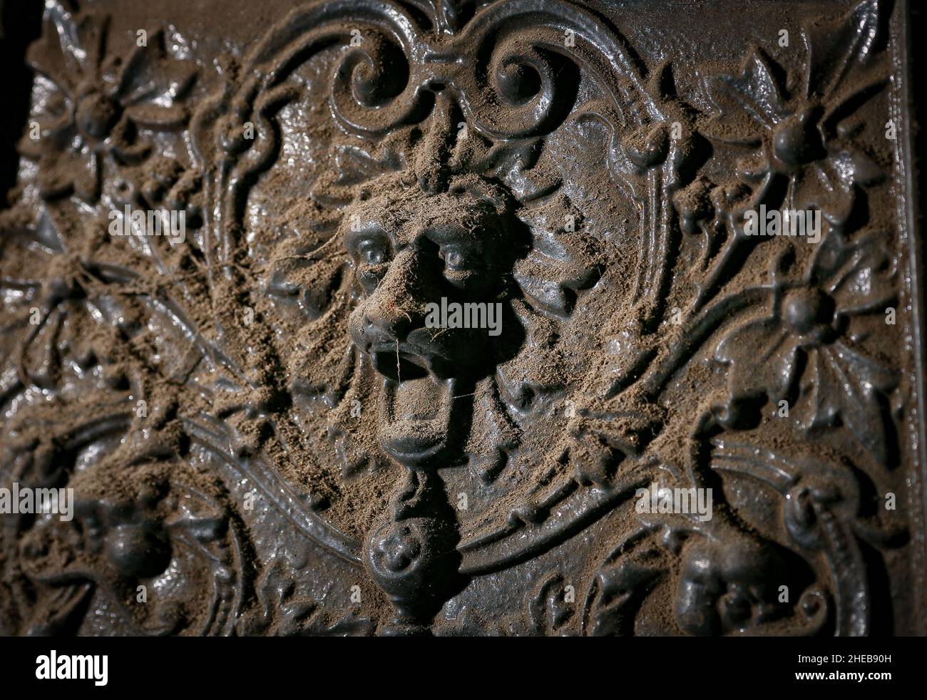 Ein dekorativer, dekorativer Löwenkopf mit ansetzenden Augen steht vor Beginn der Renovierungsarbeiten an einem antiken gusseisernen Kamin in einem alten Haus. Stockfoto