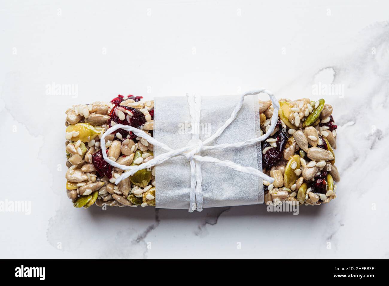 Energy Müsliriegel mit Kürbiskernen, Sesamsamen und Preiselbeeren auf weißem Marmorboden, Draufsicht. Gesundes Snack-Konzept. Stockfoto