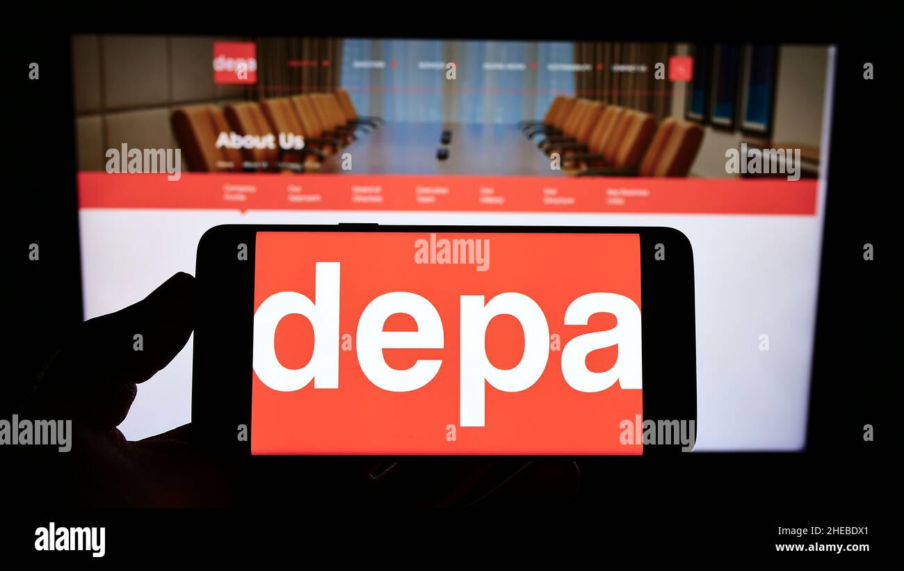 Person, die Smartphone mit dem Logo der Firma Depa PLC für den Innenausbau vor der Website hält. Konzentrieren Sie sich auf die Telefonanzeige. Stockfoto