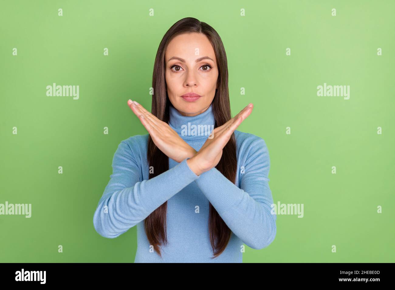 Portrait von attraktiven strengen langhaarigen Mädchen zeigt gekreuzte Hände Stopp-Zeichen isoliert über hellen grünen Hintergrund Stockfoto