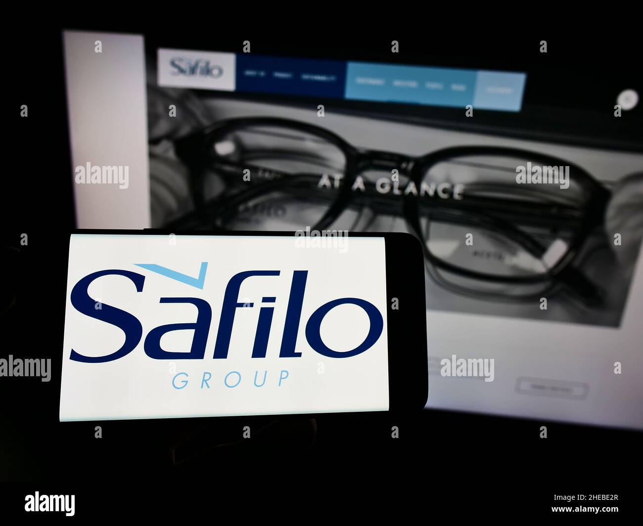 Person, die das Smartphone mit dem Logo des italienischen Brillenunternehmens Safilo Group S.p.A. auf dem Bildschirm vor der Website hält. Konzentrieren Sie sich auf die Telefonanzeige. Stockfoto