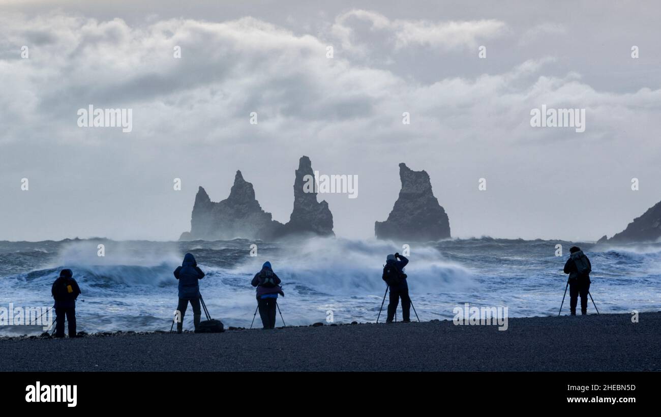 Fotografen am Strand fotografieren Felsstapel in der Nähe von Vik in Island unter einem stürmischen Himmel und vor einer brechenden Wellen Stockfoto