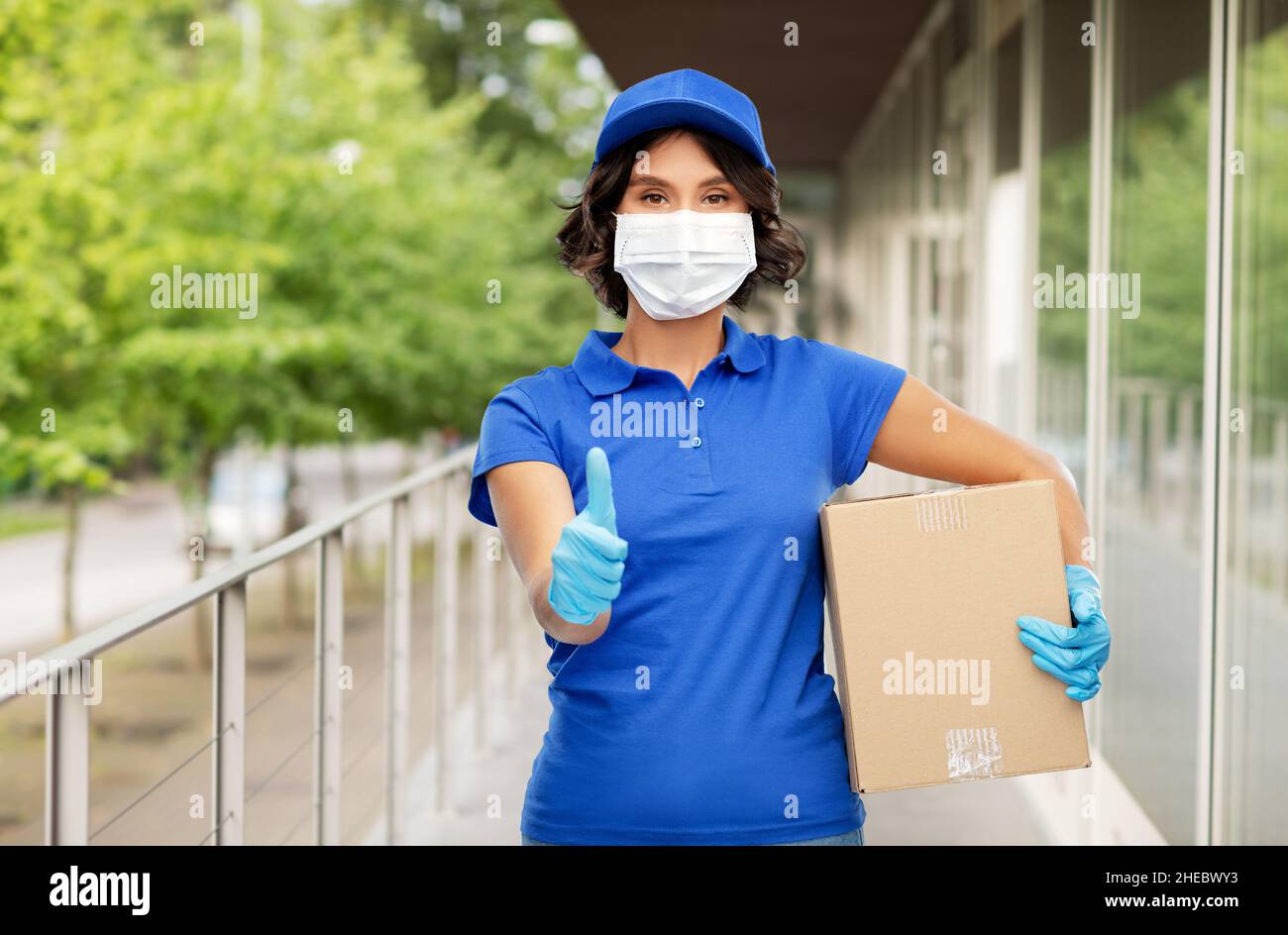 Lieferung Frau in Maske hält Paketkasten im Freien Stockfoto