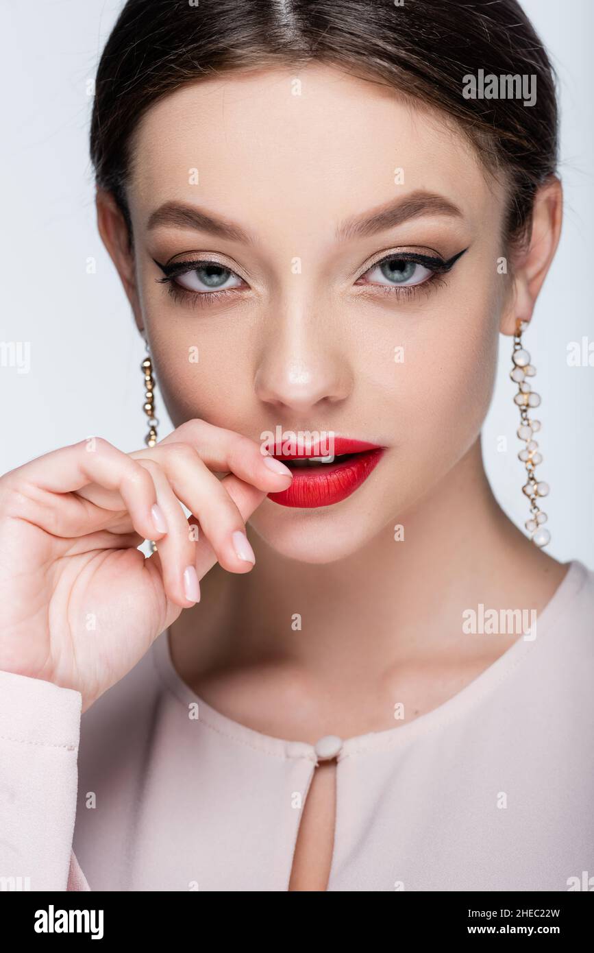 Flirty junge Frau in Ohrringen berühren Lippen isoliert auf grau Stockfoto