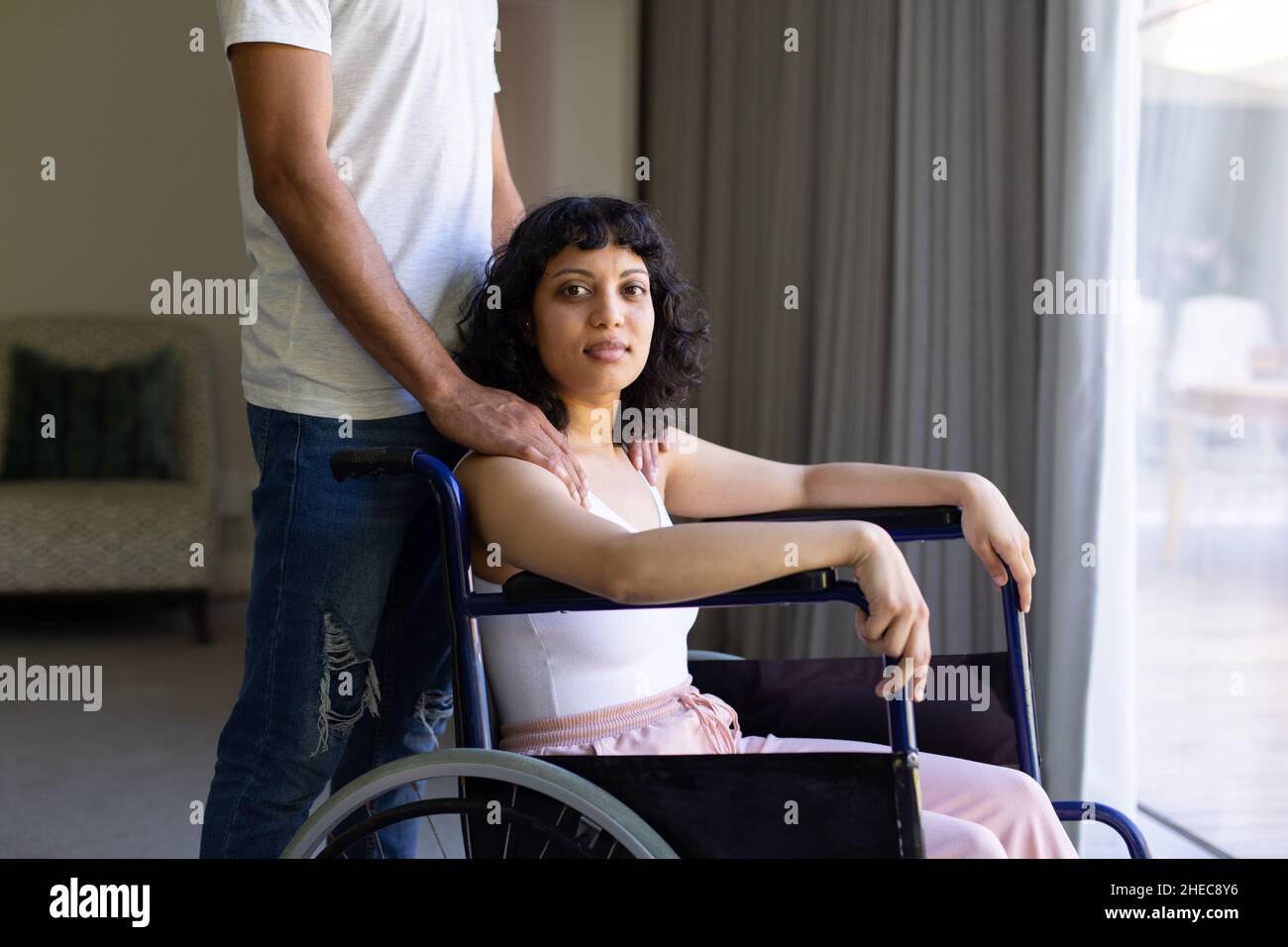 afroamerikanische behinderte Frau, die auf einem Rollstuhl sitzt, mit der Hand des Ehemanns auf ihren Schultern Stockfoto
