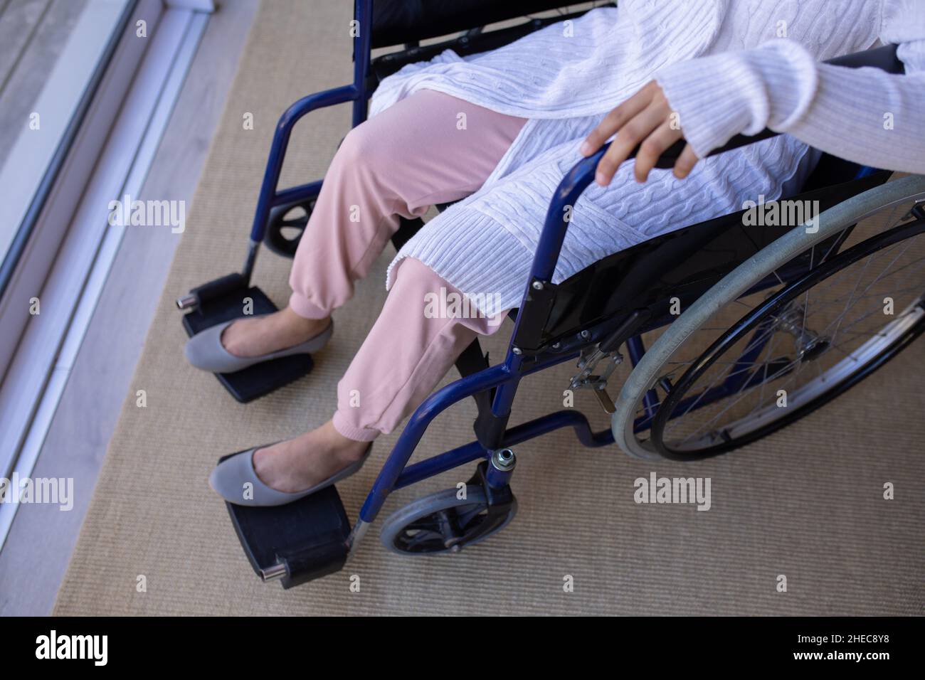 Mittelteil einer afroamerikanischen behinderten Frau, die zu Hause auf einem Rollstuhl in der Nähe des Fensters sitzt Stockfoto