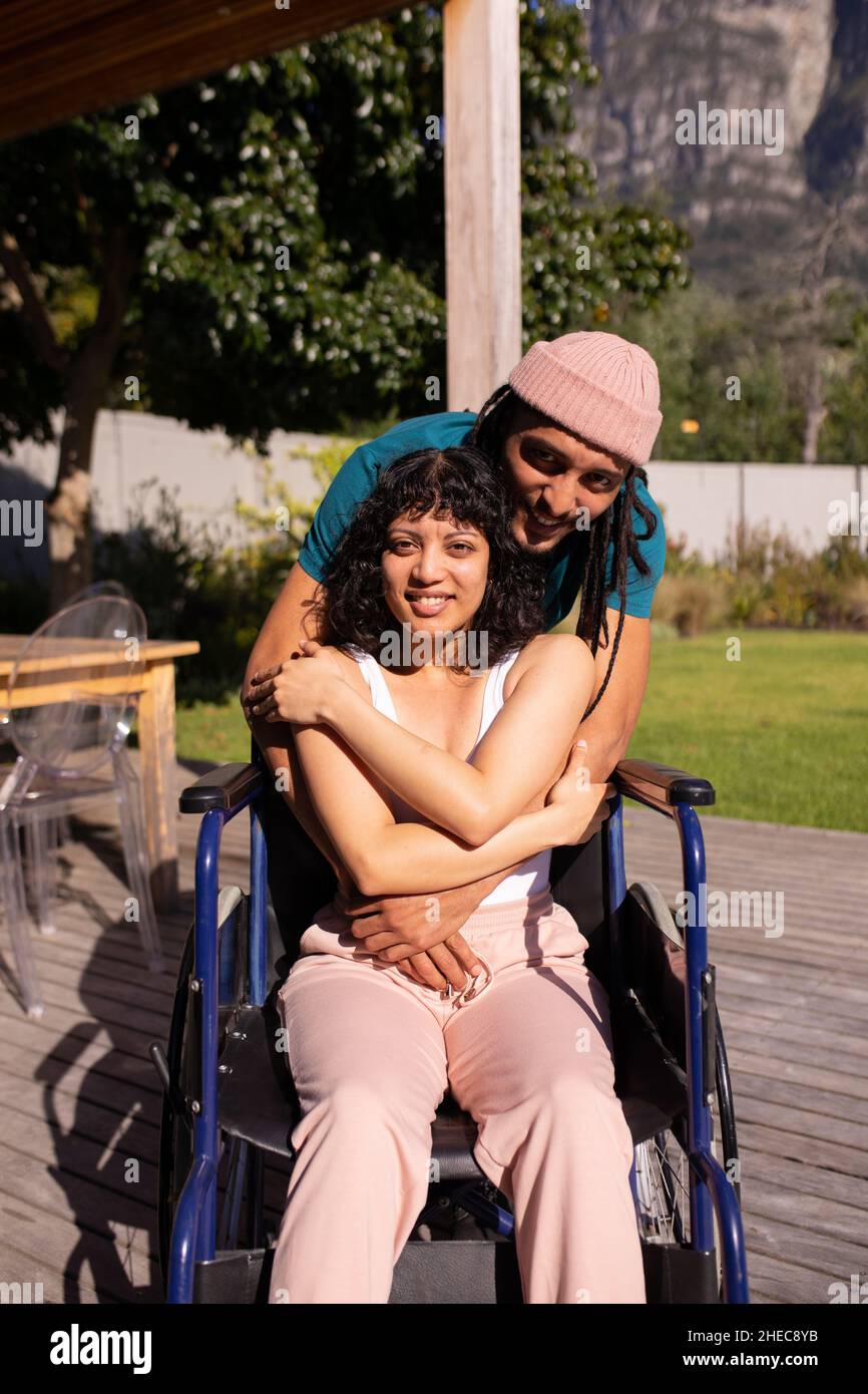 Porträt eines afroamerikanischen Mannes, der seine behinderte Frau im Freien im Rollstuhl umarmt Stockfoto