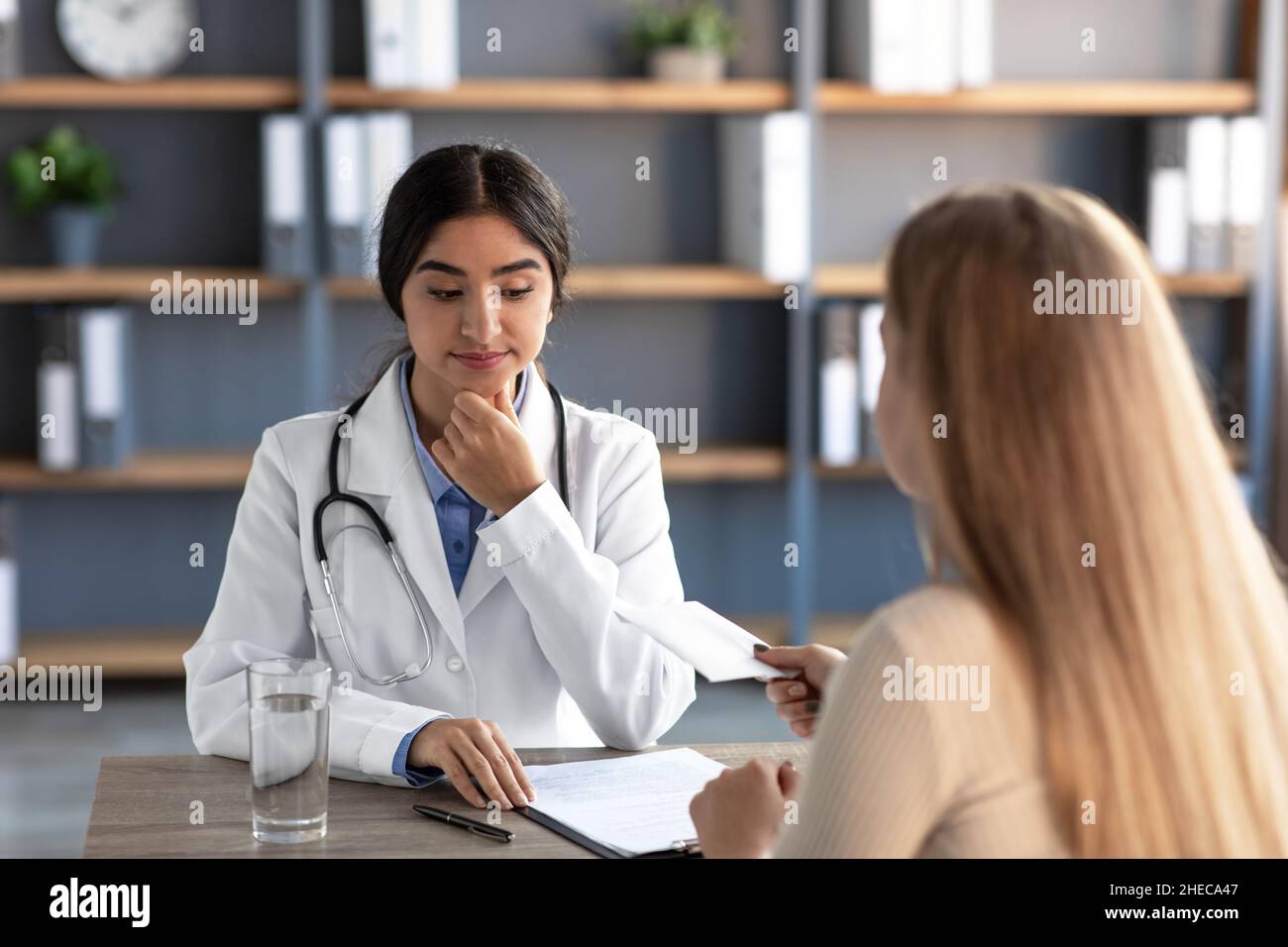 Serious Millennial indian Frau Therapeutin in Uniform, denken, schaut auf Umschlag mit Geld vom Kunden Stockfoto