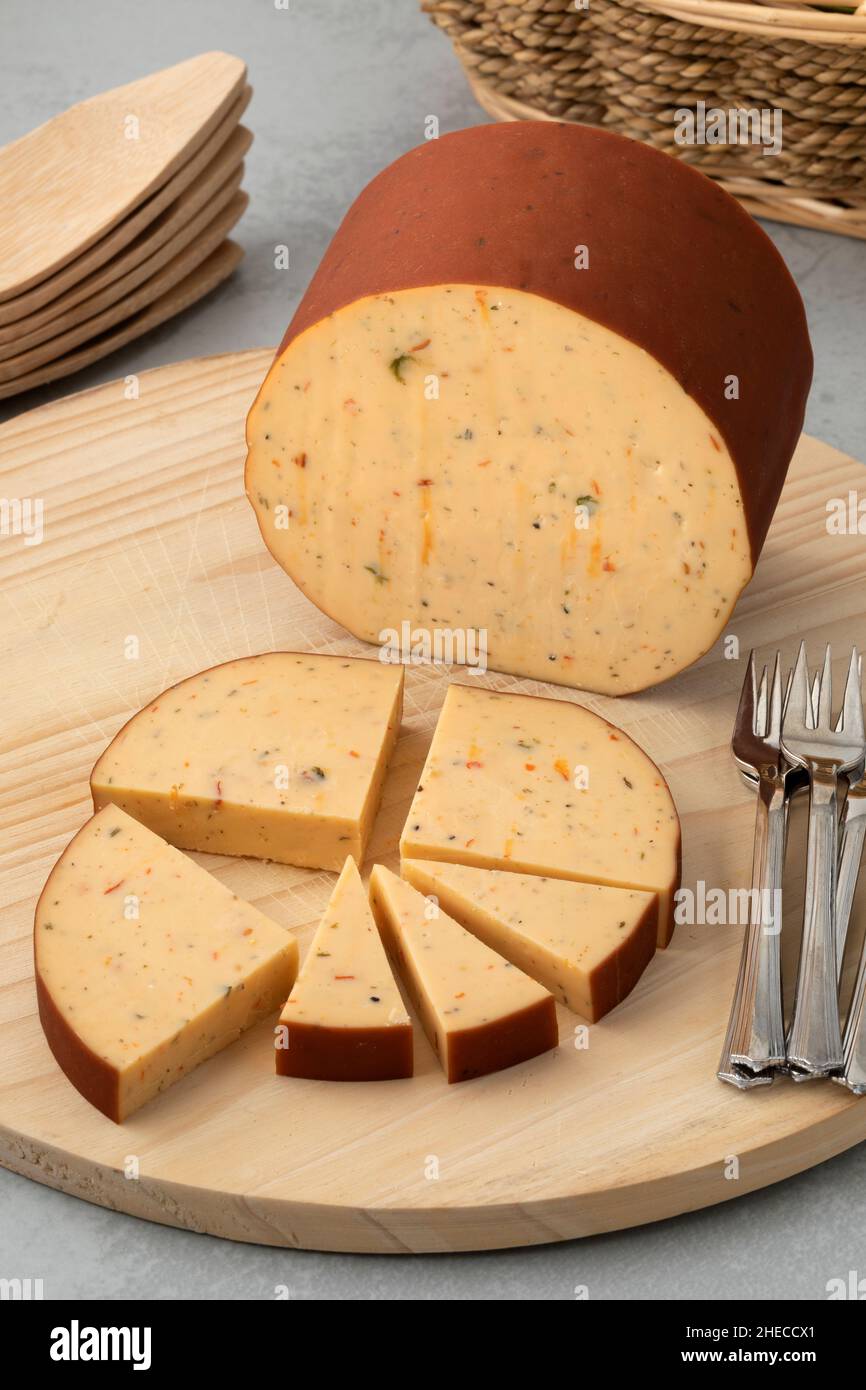 Stück und Scheibe holländischen geräucherten Käse mit einer Mischung von Kräutern auf einem Schneidebrett Stockfoto