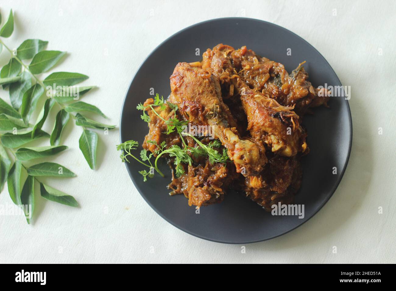 Trockener Hähnchenbraten im Kerala-Stil. Huhn in einer würzigen Soße aus Zwiebeltomaten und Gewürzen gekocht, serviert mit Hühnerschenkelstücken darauf. Schuss auf weißem Rücken Stockfoto