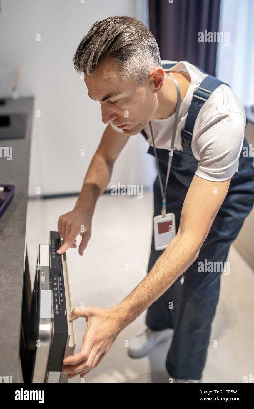 Mann, der sich zum Geschirrspüler lehnte und auf das Bedienfeld schaute Stockfoto