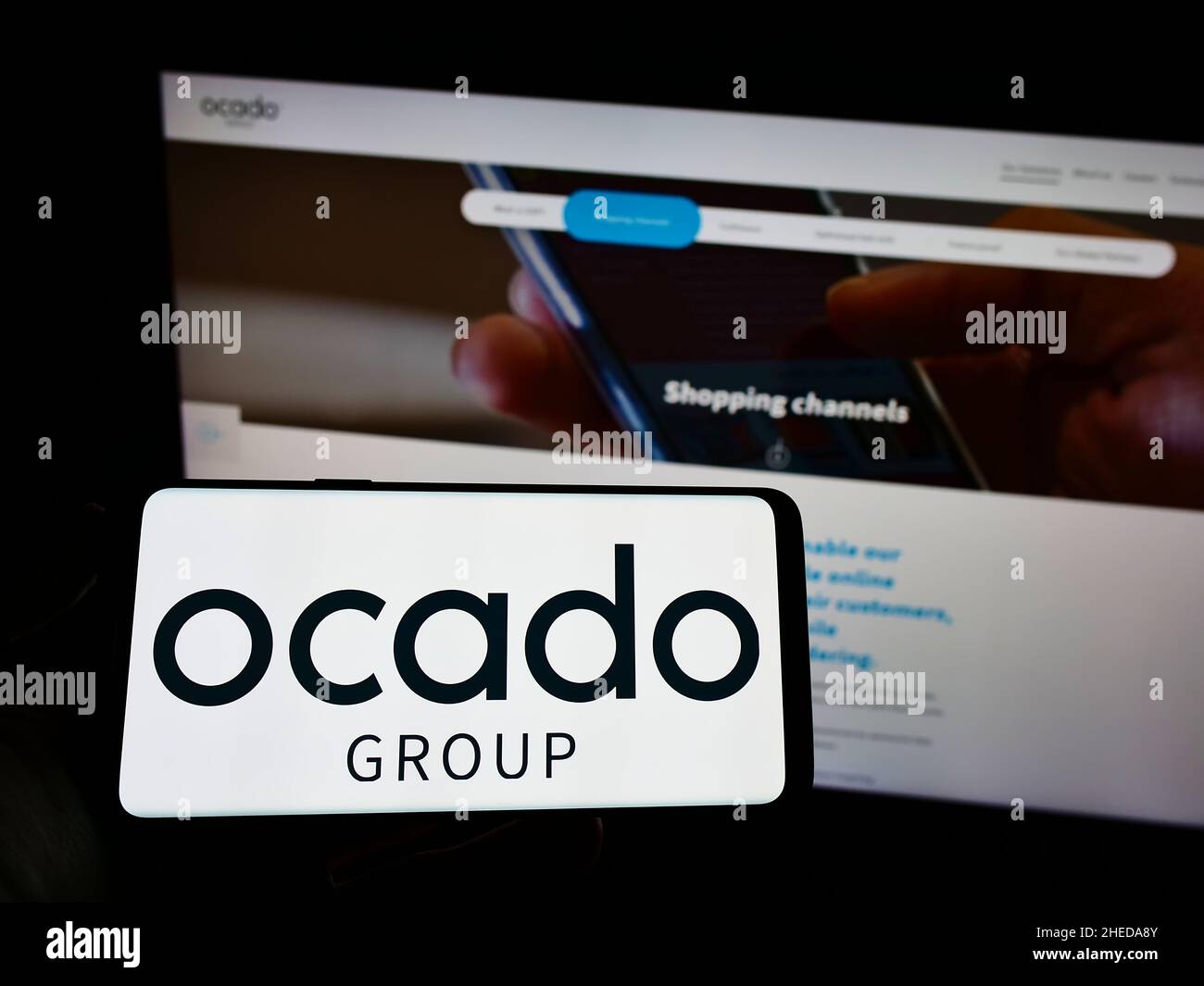 Person, die ein Smartphone mit dem Logo des britischen Einzelhandelsunternehmens Ocado Group plc auf dem Bildschirm vor der Website hält. Konzentrieren Sie sich auf die Telefonanzeige. Stockfoto