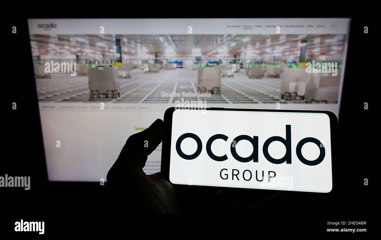 Person, die Mobiltelefon mit dem Logo des britischen Einzelhandelsunternehmens Ocado Group plc auf dem Bildschirm vor der Geschäftswebseite hält. Konzentrieren Sie sich auf die Telefonanzeige. Stockfoto