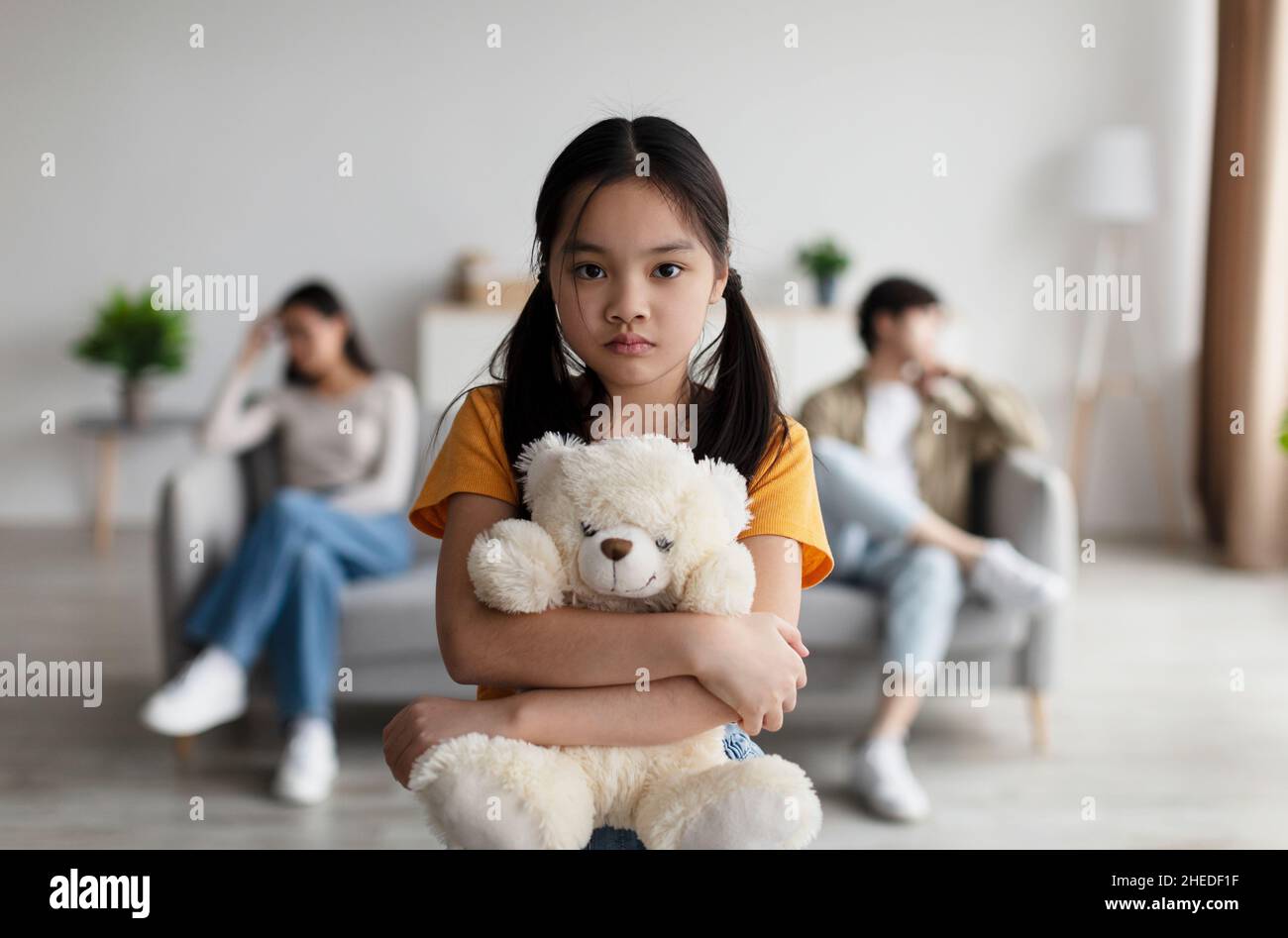 Deprimiert japanisch Adoleszenz Mädchen Umarmungen Spielzeug. Beleidigte junge Frau ignoriert Ehemann, sitzt auf dem Sofa im Wohnzimmer Stockfoto