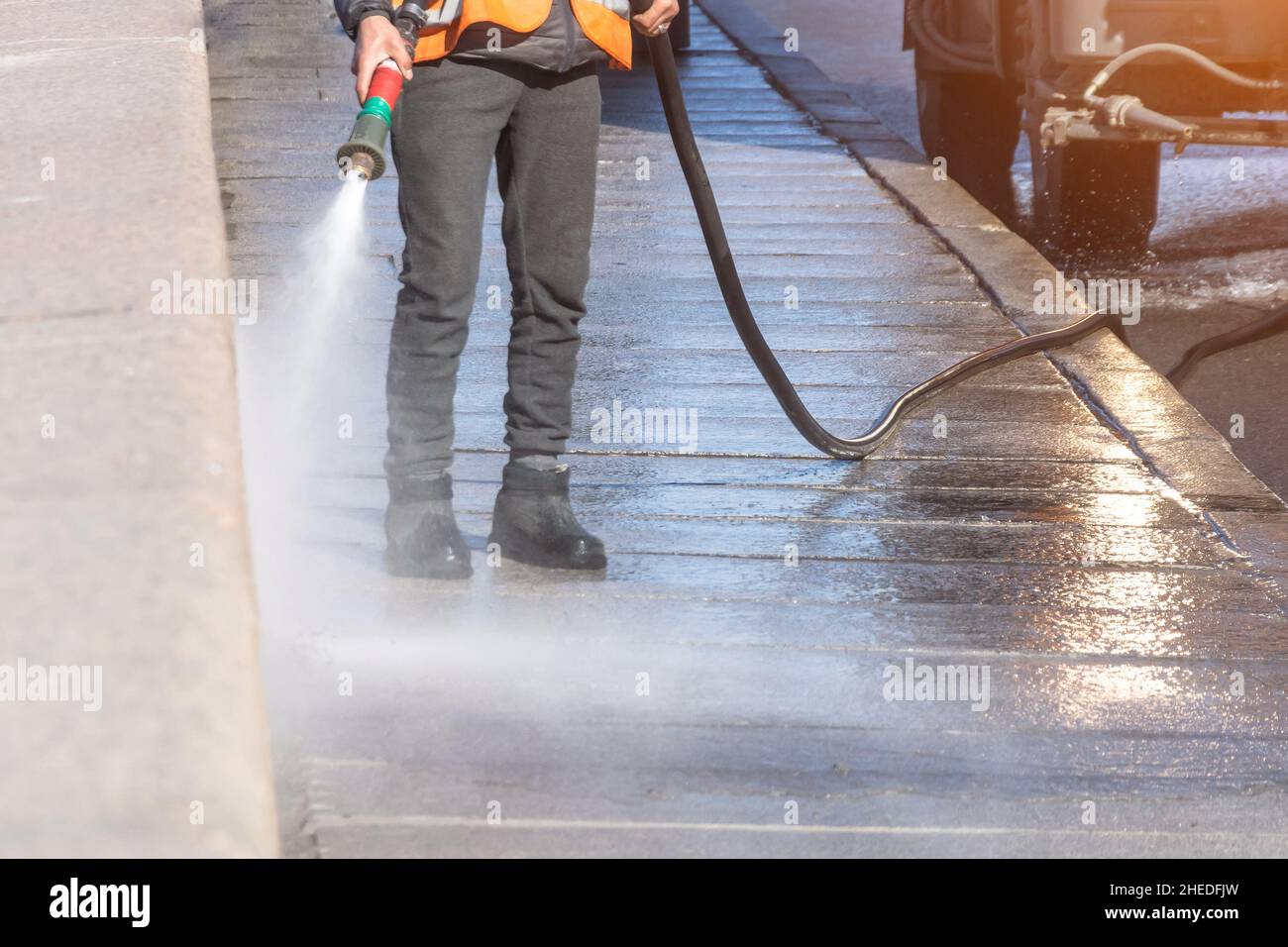 Arbeiter reinigen die Auffahrt mit Benzin Hochdruckreiniger, der den Schmutz, Granitdamm spritzt. Hochdruckreinigung Stockfoto